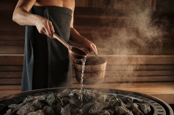 Cazo de madera vertiendo agua sobre las piedras calientes de una sauna finlandesa en un club wellness